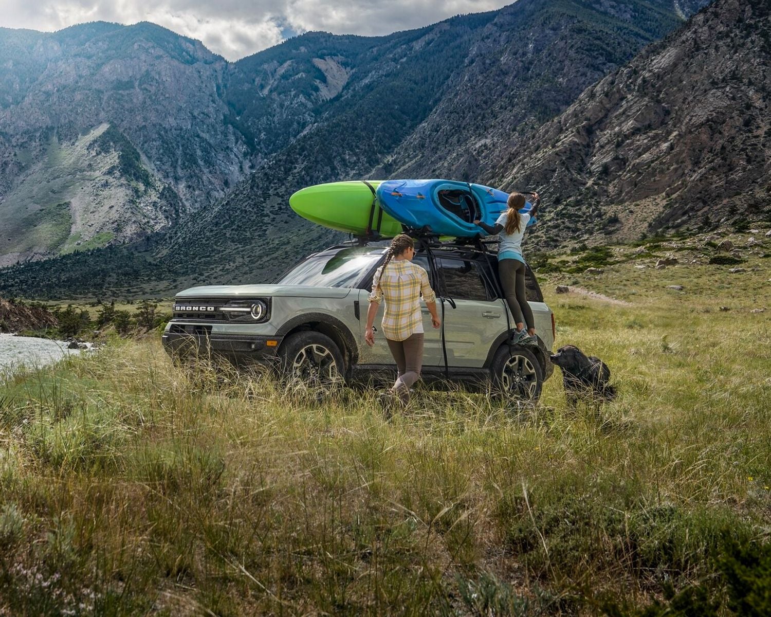 Two people are standing outside a 2024 Ford Bronco® Sport that is parked by a lake with a kayak on the roof